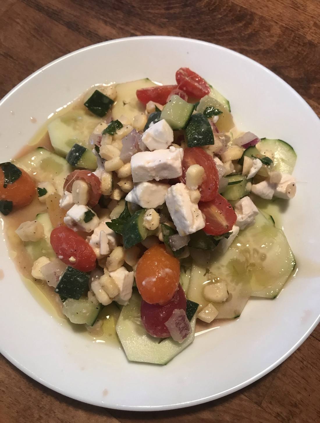 Cucumber, tomato, corn and feta salad on a white plate