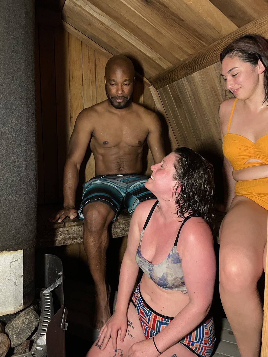 Three people talking and laughing on the benches inside the sauna